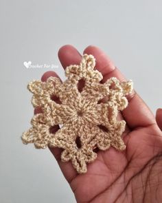 a crocheted snowflake is held in someone's hand