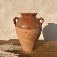 a large vase sitting on top of a wooden table next to a shadow cast wall