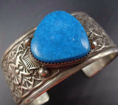 "VINTAGE NAVAJO BRACELET DESCRIPTION: This cuff features a gorgeous specimen of high blue turquoise on a cuff with intricate stamp work. The gemstone is secure in smooth bezel, on a foundation of heavy gauge vintage sterling silver. This bracelet will be a cherished addition to your collection of fine vintage Native American jewelry. MEASUREMENTS: Interior of the cuff measures 5 3/4\" with an additional 1 1/4\" slightly adjustable gap. Total circumference: 7\" Measures 2 1/2\" straight across th Southwestern Blue Cuff Jewelry, Turquoise Bangle Cuff Bracelet For Formal Occasions, Adjustable Blue Cuff Bracelet With Patina, Adjustable Blue Patina Cuff Bracelet, Blue Cuff Bracelet With Patina As A Gift, Blue Cuff Bracelet Gift, Blue Patina Cuff Bracelet As Gift, Southwestern Blue Cuff Bracelet As Gift, Blue Cuff Bracelet With Patina For Gifts