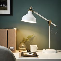 a white desk lamp sitting on top of a table next to a cup and book