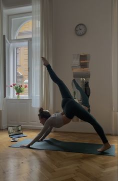 a woman is doing yoga in front of a laptop on the floor next to a window