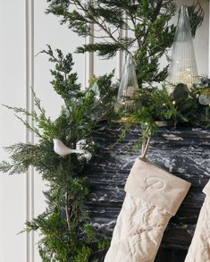 two stockings hanging from a mantel decorated with greenery