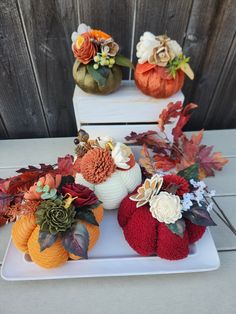 pumpkins and flowers are sitting on a white platter next to other fall decorations