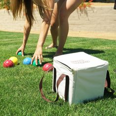 a woman bending over to pick up some balls from the grass in front of her