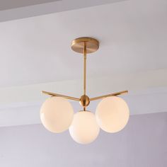 three white balls are hanging from a brass ceiling light in a room with gray walls