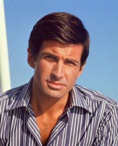 a man wearing a striped shirt sitting in front of a wind turbine and looking at the camera