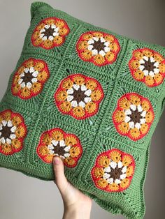 a hand holding a green crocheted pillow with orange and brown flowers on it