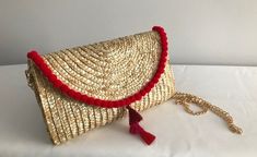 "From an evening cocktail party to a fun beach day, this straw clutch makes a graceful accessory to carry. Perfect for a summer statement. Red pom poms with red/pink tassel center.  Comes w/ removable gold chain strap that can be worn as a crossbody or shoulder strap. NOTE:  Pom pom embellishment is only on the top fold of the clutch (NOT on the back or other edges of the clutch) Details: Clutch Size: 6.5\" x 10\" Shoulder strap: 47\" gold Face material: wheat straw Lining material: polyester and cotton" Chic Straw Bag With Tassels, Chic Gold Straw Bag For Summer, Red Beach Bag With Tassels, Gold Straw Bag For Summer Evenings, Summer Evening Clutch With Woven Details, Chic Red Woven Straw Bag, Chic Clutch With Tassels, Chic Evening Straw Bag For Summer, Gold Straw Evening Bag For Summer