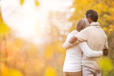 a man and woman embracing each other in front of trees with yellow leaves on them