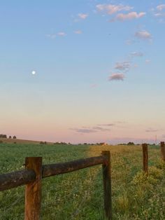 a fence in the middle of a grassy field with a full moon in the distance