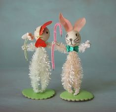 two bunny figurines are standing next to each other on green bases, one holding a candy cane