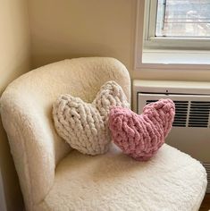 a white chair with two knitted hearts sitting on it's back in front of a window