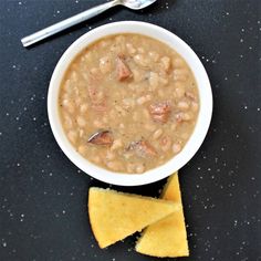 a white bowl filled with beans and cheese next to crackers on a black surface