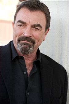 a man with a goatee and beard smiling at the camera, wearing a black suit