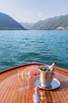 two glasses of wine and an ice bucket on a boat with mountains in the background