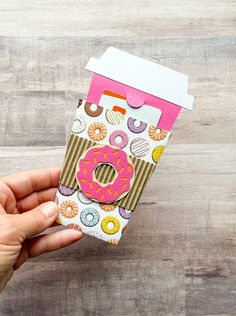 a hand holding up a paper cup with donuts on it and a pink lid