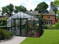 a green house in the middle of a lush green yard with potted plants on either side