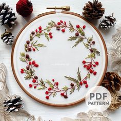 a cross stitch pattern with red berries and pine cones on white paper surrounded by christmas decorations