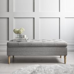 a white room with a bench and flowers on it's end table in front of a paneled wall