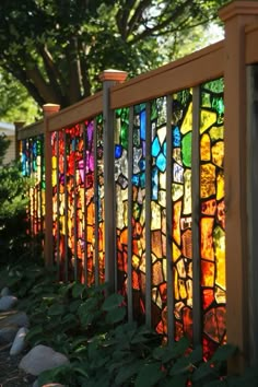 a fence made out of stained glass sitting in front of a tree and bushes with rocks on the ground