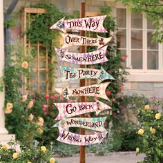 a wooden pole with signs on it in front of some flowers and bushes, that say'this way over there is somewhere tea party go back wonderful wrong