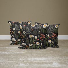 three black floral pillows sitting on top of a wooden floor next to a brown wall