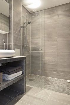 a bathroom with gray tiles and white fixtures, including a shower stall that has towels on the shelf