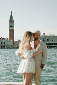 a man and woman standing next to each other near the water