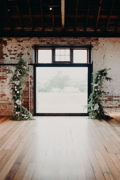 an empty room with wooden floors and brick walls is decorated with greenery for a wedding ceremony