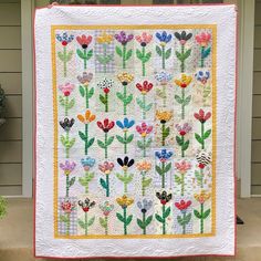 a quilted wall hanging on the side of a house with colorful flowers in it