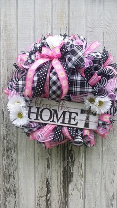 a wreath that says home is decorated with pink, white and black ribbons on a wooden fence