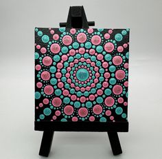 a small easel with an abstract painting on it's sides and the top half painted in pink, blue and green