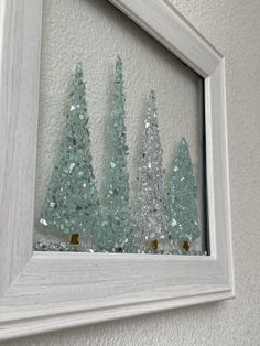 three small trees are displayed in a white frame on the wall behind it is glittered glass