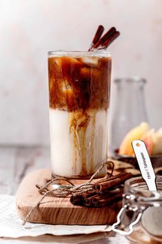 an iced drink with cinnamon sticks in it sitting on a wooden cutting board next to other items