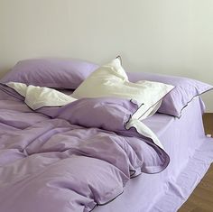 an unmade bed with purple sheets and pillows