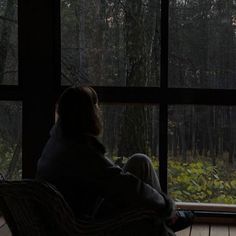 a person sitting in a chair looking out a window at the woods outside and trees