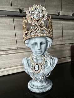 Add a touch of elegance to your space with our hand-painted Bust Statue with Crown. Available in silver or gold accents, each bust features rhinestones and a unique neck piece. The removable hand made metal crown is adorned with more rhinestones for a regal look. Made of poly resin and perfect for any home or office setting. Silver Crown -This bust has silver accents. She has rhinestones and a pink heart around her neck. Her metal crown is hand made, removable and is painted white and black with Pink Heart Necklace, Bust Statue, Metal Crown, Office Setting, Silver Crown, Neck Piece, Gold Crown, Pink Accents, Silver Accents