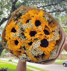 a bouquet of sunflowers is being held by someone's hand in front of a tree