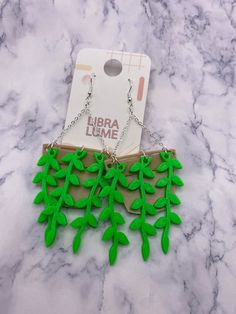 a pair of green leafy earrings on a white marble counter with a card for purchase