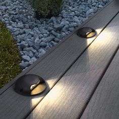 two lights on the side of a wooden bench in front of some rocks and grass