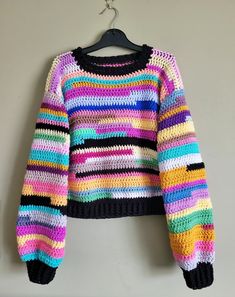 a multicolored sweater hanging on a hanger next to a white wall with a black hook