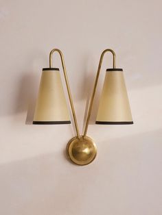 two brass lamps with black shades on the wall