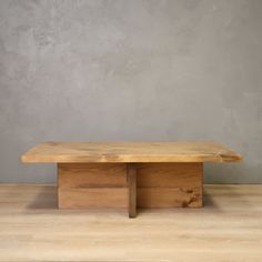 a wooden bench sitting on top of a hard wood floor next to a gray wall