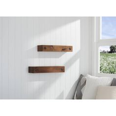 three wooden shelves on the wall above a bed in a room with white walls and windows