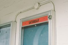 an orange sign that reads saturday on the side of a white building with blue windows