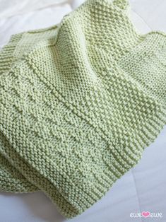 a green knitted blanket laying on top of a white bed sheet with the cover pulled down