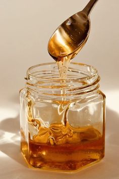 a spoon is pouring honey into a jar