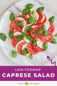 a white plate topped with sliced tomatoes and basil on top of a marble countertop