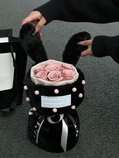 a person holding a bouquet of pink roses in a black and white hat with ribbon