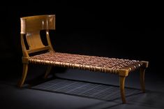 a wooden chair sitting on top of a black floor next to a table with a woven seat